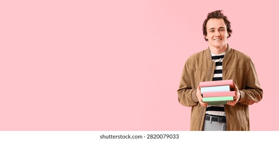 Smiling young man holding a stack of colorful books, education and learning concept, isolated on a pink background with copy space