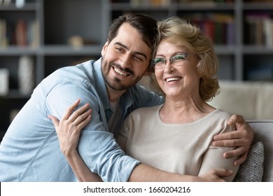 Smiling Young Man Hug Middle-aged Optimistic Mother Look In Distance Dreaming Or Visualizing Together, Happy Senior 70s Mother Embrace Adult Grown-up Son Enjoy Family Weekend At Home, Vision Concept