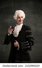 Smiling Young Man In Image Of Amadeus Mozart, Medieval Person Isolated On Dark Vintage Background. Retro Style, Comparison Of Eras Concept. Elegant Male Model As Historical Character, Music Composer