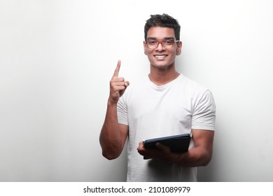 Smiling young man of Indian origin holding a tablet computer shows his pointed finger up - Powered by Shutterstock