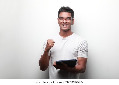 Smiling young man of Indian origin holding a tablet computer shows cheering gesture - Powered by Shutterstock