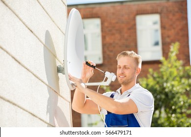 Smiling Young Man Installing TV Satellite Dish To Wall
