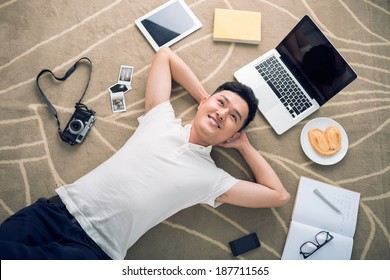 Smiling young man lying on the floor surrounded with his favorite things