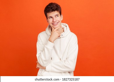 Smiling young man with peaceful face thinking over plans for future holding his chin, thoughtful teenager dreaming about good job. Indoor studio shot isolated on orange background - Powered by Shutterstock