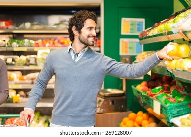 Smiling Young Man Picking Up Vegetables In A Grocery Store