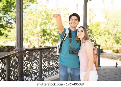 Smiling young man pointing and showing girlfriend something while traveling together