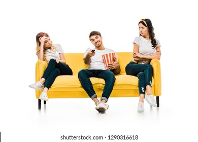 Smiling Young Man With Popcorn Box And Remote Controller Watching Tv While Bored And Upset Woman Sitting On Couch Isolated On White