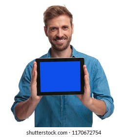 smiling young man presenting the blank screen of his tablet on white background