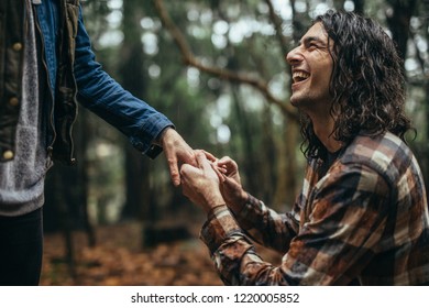 Smiling Young Man Putting Engagement Ring On Woman's Hand Outdoors Under The Rain. Cheerful Guy Making Marriage Proposal To Girlfriend At Park.