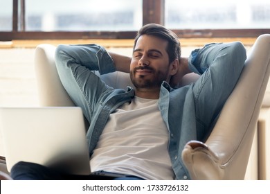 Smiling Young Man Relax In Comfortable Armchair At Home Take Nap Daydream Distracted From Computer Work, Happy Millennial Male Sit Rest In Cozy Chair In Living Room Enjoy Peace, Stress Free Concept