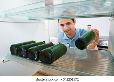 Smiling Young Man Removing Beer Bottle From Refrigerator At Home