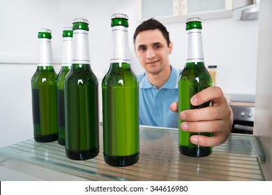 Smiling Young Man Removing Beer Bottle From Refrigerator At Home