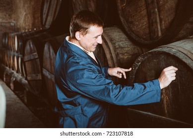 Smiling young man in robe checking ageing barrel process of wine