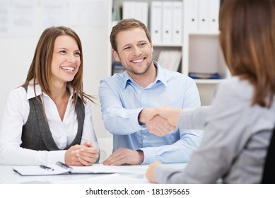 Smiling young man shaking hands with an insurance agent or investment adviser as he sits in a meeting with his wife in her office