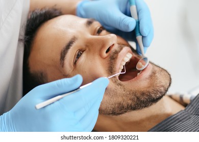 Smiling Young Man Sitting In Dentist Chair While Doctor Examining His Teeth