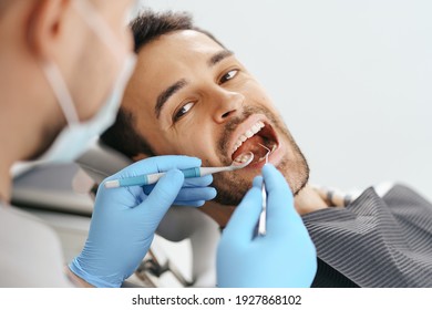 Smiling Young Man Sitting In Dentist Chair While Doctor Examining His Teeth