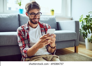 Smiling young man sitting on floor and texting friend