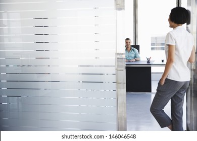 Smiling Young Man Talking To Woman Standing In Doorway At His Office