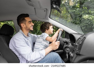 Smiling Young Man Teaching Little Child To Drive Car In Summer, Boy Hold Steering Wheel And Look At Road, Profile, Outdoor, Copy Space. Dad And Son Enjoy Time Together At Weekend And Driving Lesson