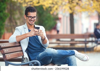 Smiling Young Man Texting On The Cellphone