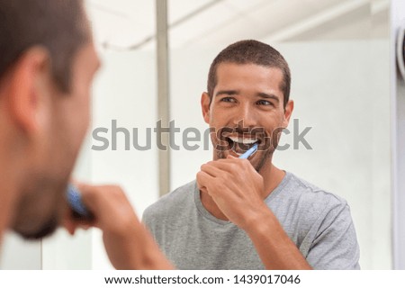 Smiling young man with toothbrush cleaning teeth and looking mirror in the bathroom. Handsome man brushing his teeth in morning in bathroom. Happy guy in pajamas brushing teeth before going to sleep. Foto stock © 