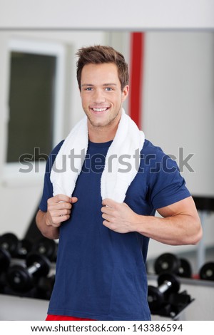 Smiling young man training in the gym with towel around his neck