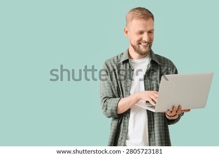 Smiling young man using laptop on blue background