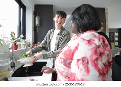 Smiling young man washing lettuce and talking to senior woman in kitchen - Powered by Shutterstock