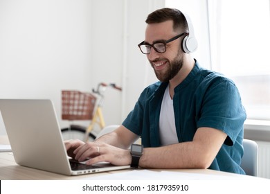 Smiling young man wearing glasses and headphones looking at laptop screen, working on online project, sitting at work desk in modern office, student listening to music or web course lecture - Shutterstock ID 1817935910