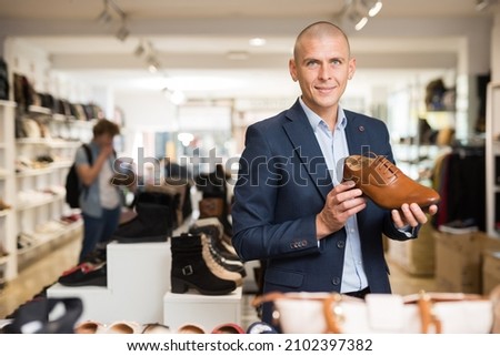 Smiling young man wearing in suit looking for comfortable classic shoes in shoe store.