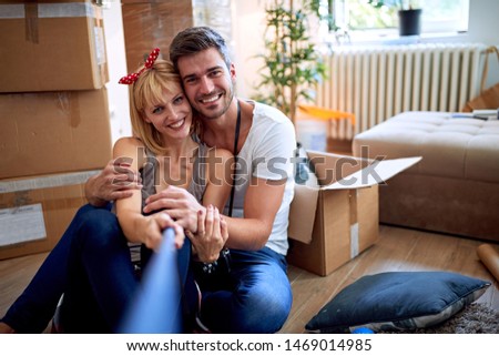 Smiling young man and woman having fun at new home and taking selfie.
