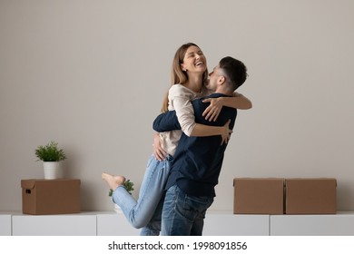 Smiling Young Man And Woman Hug Relax On Moving Day Buying First Shared House Together. Happy Caucasian Couple Renters Tenants Embrace Celebrate Moving Relocation To New Own Home. Rent Concept.