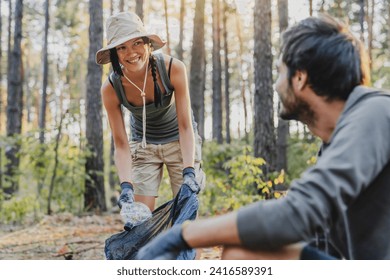 Smiling young man and woman picking up trash and plastic from forest in bags. Volunteers caucasian eco-activists collecting plastic bottles to clean up the woods and do recycling - Powered by Shutterstock