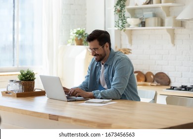 Smiling young man working on laptop in modern kitchen, checking email in morning, writing message in social network, happy young male using internet banking service, searching information - Powered by Shutterstock