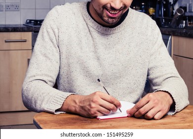 Smiling Young Man Is Writing In His Kitchen