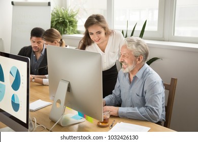 Smiling Young Manager Helping Senior Worker With Funny Computer Work In Office, Mentor Teacher Training Happy Older Employee At Workplace, Colleagues Of Different Age Laughing Looking At Pc Monitor