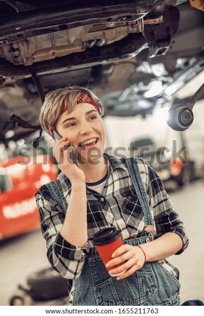 Smiling\
young mechanic using her gadget at coffee\
break