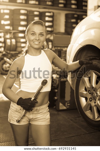 Smiling young mechanic woman working on car wheel\
in service point