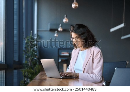 Smiling young middle eastern business woman specialist working focused on laptop computer. Middle aged latin hispanic investor, bank worker using pc for analysing, network at workplace desk in office