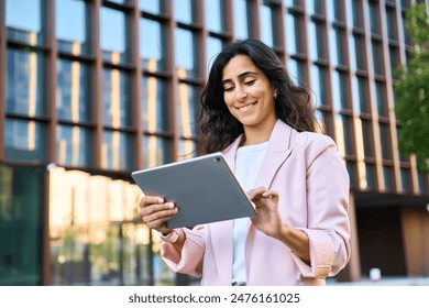 Smiling young middle eastern Israel businesswoman using tablet pc application for online remote work at office business building outdoors. Indian or arabic woman holding digital computer. Copy space - Powered by Shutterstock