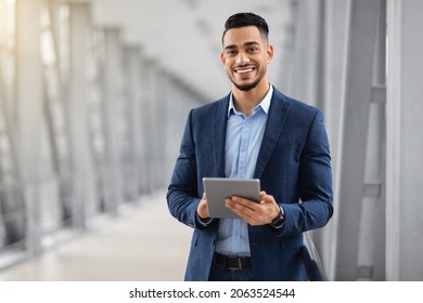 Smiling Young Middle Eastern Man With Digital Tablet In Hands Posing At Airport Terminal, Successful Millennial Arab Businessman Using Tab Computer While Waiting For Flight Boarding, Copy Space - Powered by Shutterstock