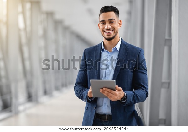 Smiling Young Middle Eastern Man With Digital\
Tablet In Hands Posing At Airport Terminal, Successful Millennial\
Arab Businessman Using Tab Computer While Waiting For Flight\
Boarding, Copy Space