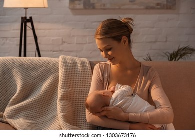 Smiling Young Mother Breastfeeding Baby At Night