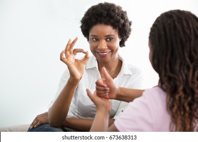 Smiling Young Mother Learning Sign Language To Talk With Her Hearing Impairment Daughter - Powered by Shutterstock