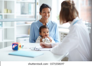 Smiling Young Mother Sitting Together With Her Baby And Talking To The Doctor During Their Visit At Hospital