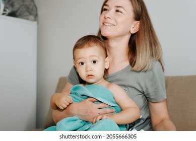 Smiling Young Mother Wiping Her Baby With Towel After Bathing At Home Indoors. Mom And Cute Little Boy Looking At Camera With Big Eyes. Motherhood, Childcare, Clean And Healthy Concept.