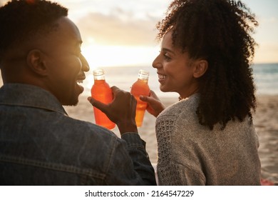 Smiling young multiethnic couple drinking juice on a beach at sunset - Powered by Shutterstock