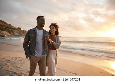 Smiling young multiethnic couple walking along a beach at sunset - Powered by Shutterstock