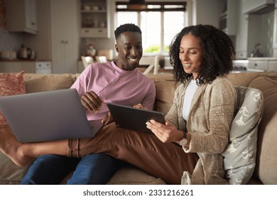 Smiling young multiracial couple using a tablet and laptop on their sofa - Shutterstock ID 2331216261
