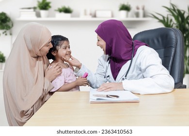 Smiling young muslim doctor wearing hijab checking girl child at modern clinic. Friendly female pediatrician examine young kid patient with her mother. - Powered by Shutterstock